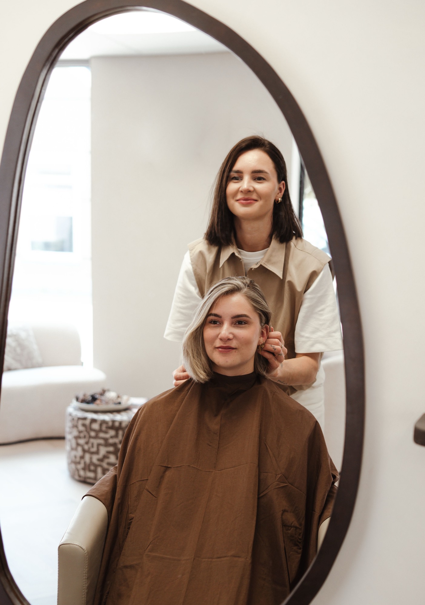 Amy en een klant met zacht blond haar, gespiegeld in de ovale spiegel van de salon